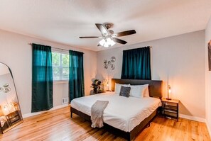 A bedroom with a bed, a ceiling fan, a bedside table, and a window with curtains. - NEW! Movies, Games, and Backyard Hangs, 4 Bedrooms (Northglenn)