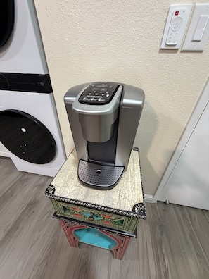 A coffee maker on a small table with a decorative box underneath.