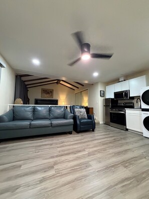 A modern living room with a grey leather sofa, a black armchair, and a ceiling fan.
