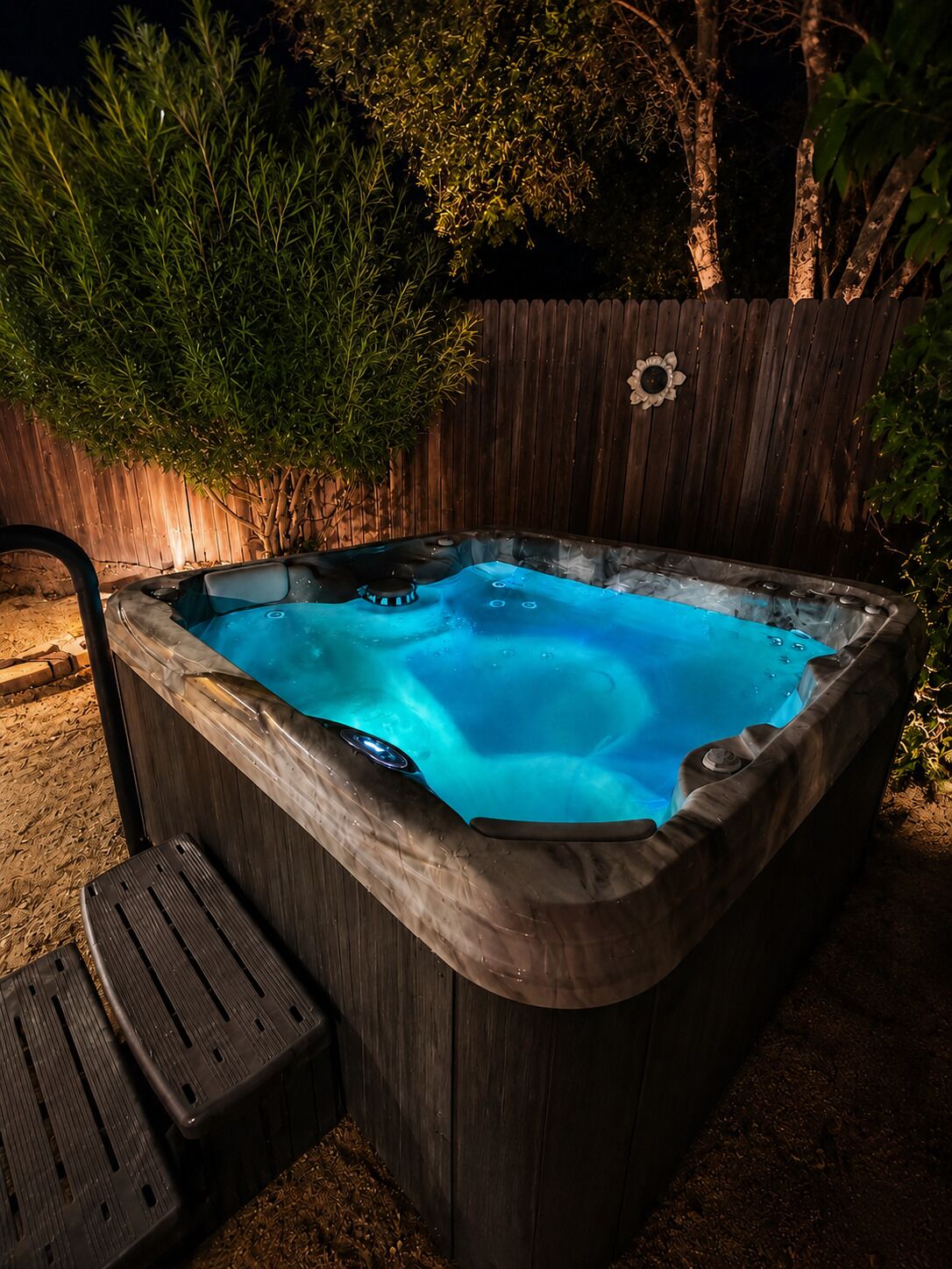 Un bain à remous avec une structure extérieure en bois, entouré d’une clôture en bois et de verdure.