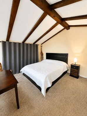 A bedroom with a bed, a nightstand, a desk, and a window with curtains.