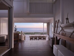 Un ampio balcone con pavimento in legno, un'area salotto con sedie e vista sull'oceano.