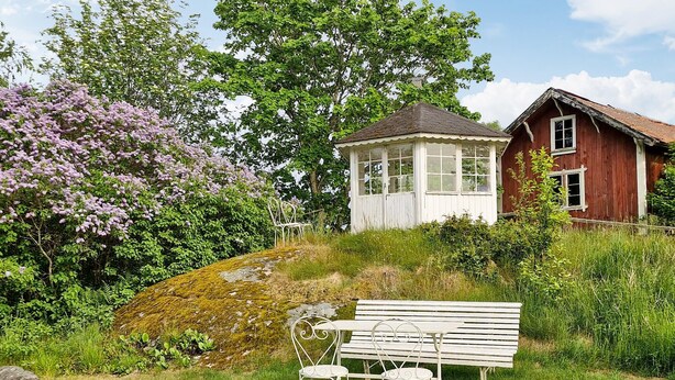 A rustic wooden house with a white porch, a bench, and two chairs in front.
