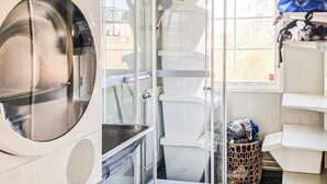 A laundry room with a front-loading washing machine, stacked dryers, and a window with a view of trees.