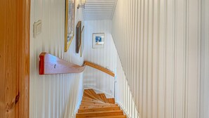 A wooden staircase with a handrail, white walls, and a framed picture on the wall.