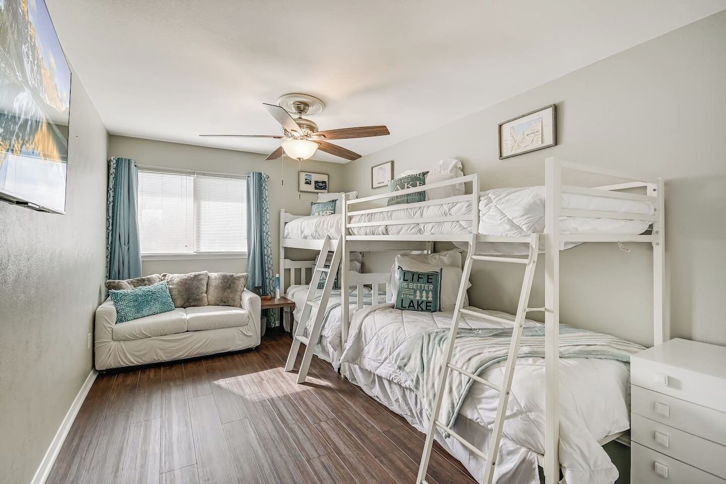 A room with bunk beds, a sofa, a ceiling fan, and a window with curtains.