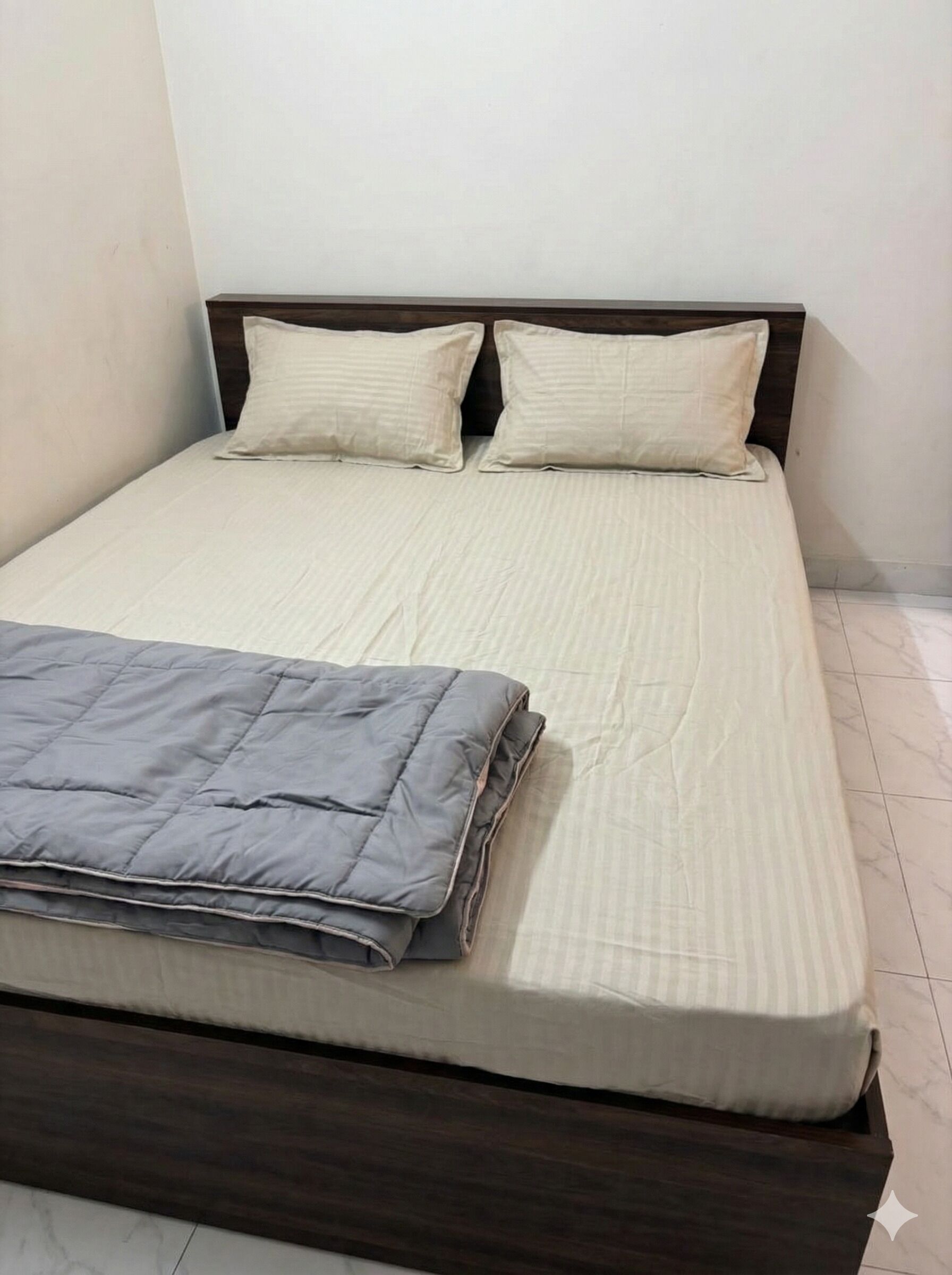 Un lit simple avec une tête de lit en bois, deux oreillers et une couverture pliée.