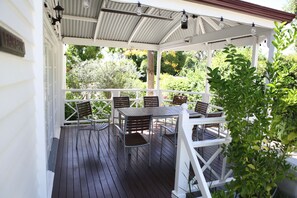 A covered outdoor deck with a table and chairs, surrounded by white railings and greenery.