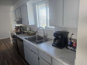 A modern kitchen with white cabinets, a double sink, a coffee maker, and a window providing natural light.