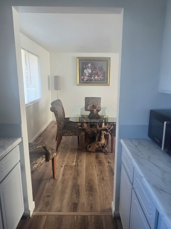 A dining area with a wooden table and chairs, a framed floral artwork on the wall, and a television on a cabinet.