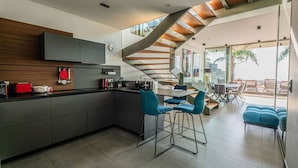 Una cocina moderna con una isla central, un comedor con sillas azules y una escalera que lleva a un patio exterior.