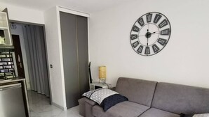 Een moderne woonkamer met een grijze bank, een grote wandklok en een bijzettafeltje met een lamp.