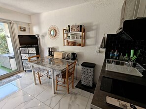 A modern kitchen with a marble countertop, wooden chairs, a coffee machine, and a black stove. - JARDINS D'YS Studio for 2 people with air conditioning (LES ISSAMBRES)