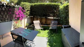 Een terras met een tafel en twee stoelen, omgeven door een houten hek en weelderige begroeiing.