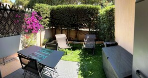 A patio with a table and two chairs, surrounded by a wooden fence and lush greenery. - JARDINS D'YS Studio for 2 people with air conditioning (LES ISSAMBRES)