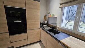 Eine moderne Küche mit Holzausstattung, einer schwarzen Arbeitsplatte, einem eingebauten Ofen und einem Fenster mit Blick ins Freie.