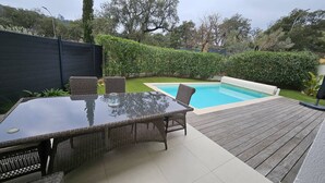 Ein Garten mit Pool, einem Glastisch, Korbstühlen und einer Holzterrasse.