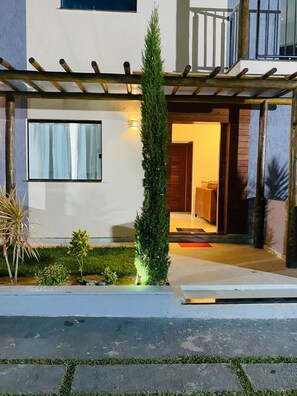 Ein modernes, zweistöckiges Haus mit überdachter Veranda, kleinem Garten und einem sichtbaren Inneneingang.