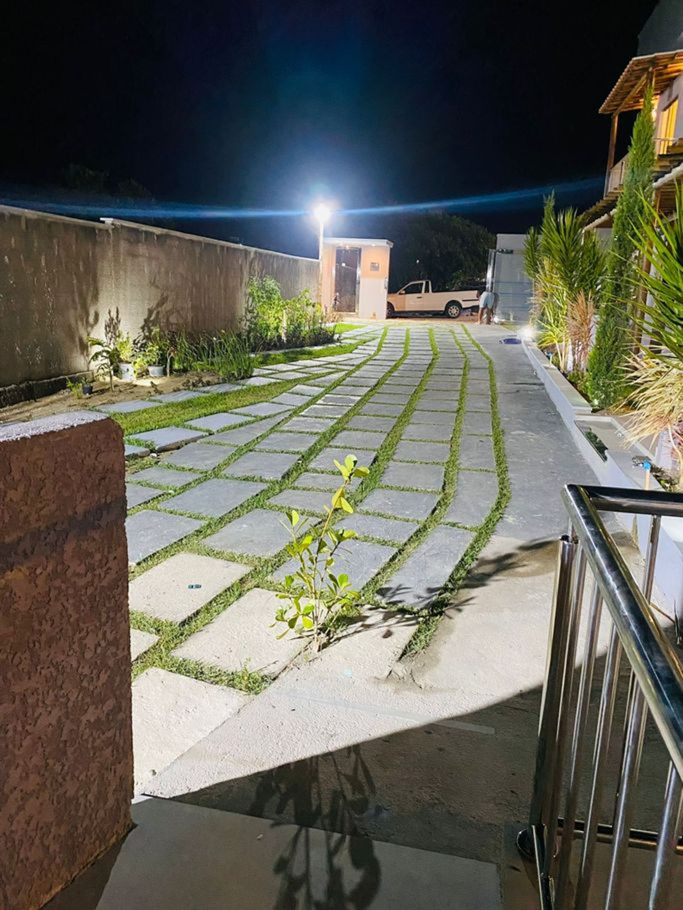 Ένα ασφαλτοστρωμένο μονοπάτι που οδηγεί στην είσοδο ενός κτιρίου τη νύχτα, με ένα όχημα σταθμευμένο κοντά.