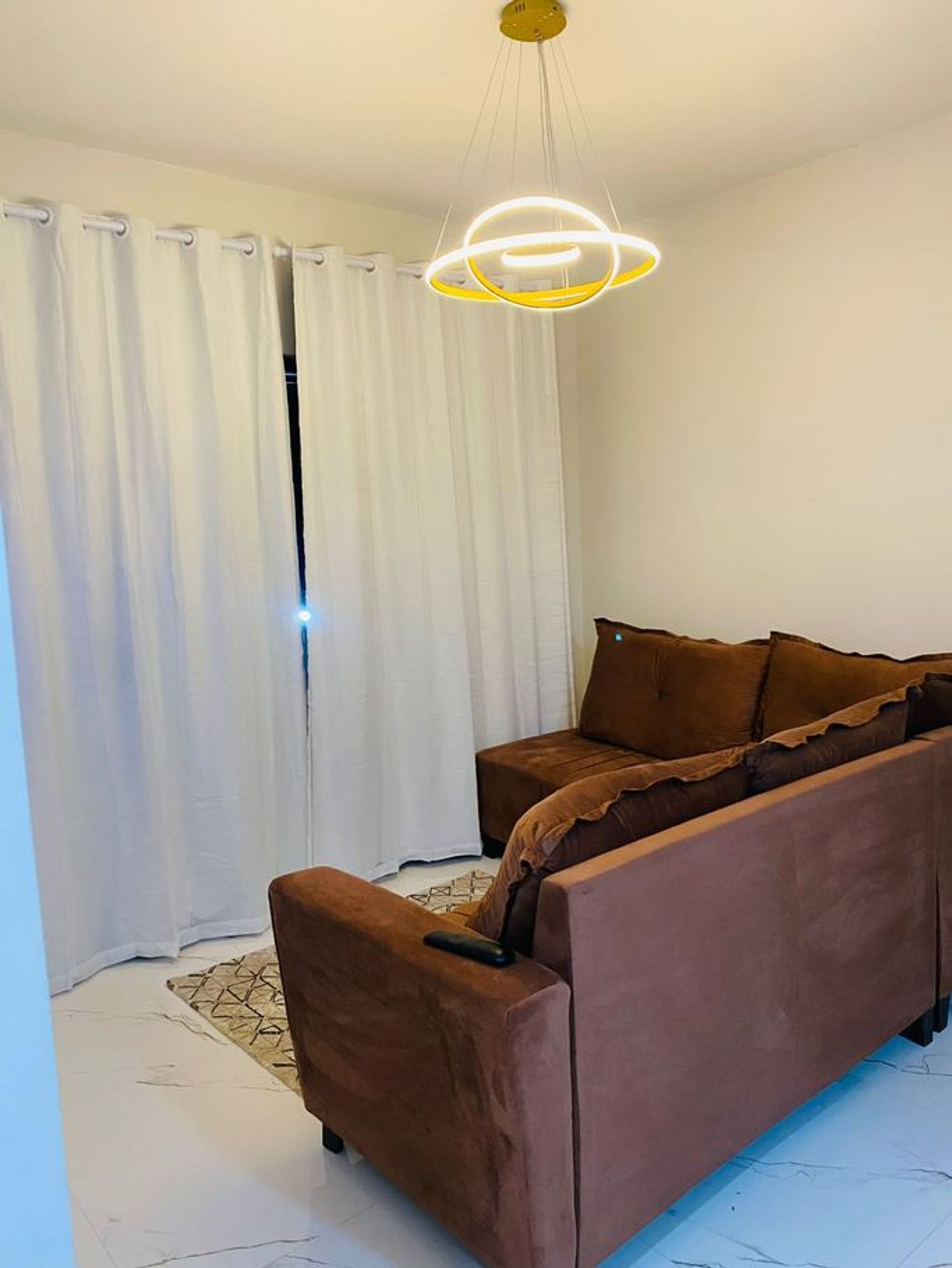A modern living room with a brown sofa, white curtains, and a unique ceiling light fixture.