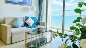 Ein modernes Wohnzimmer mit einer Couch, einem Glastisch und Blick auf das Meer durch große Fenster.