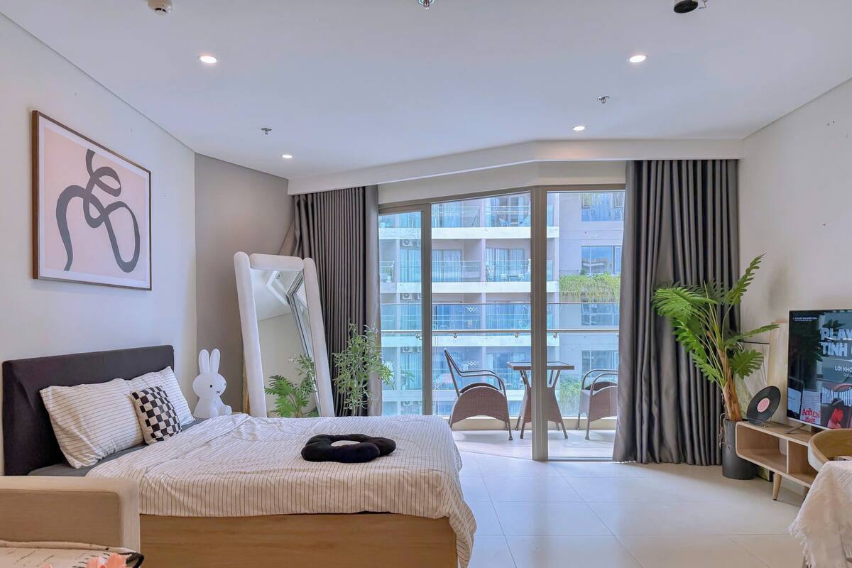 Una habitación de hotel moderna con cama, un espejo grande, televisión, balcón con vista a la ciudad y un área de comedor.
