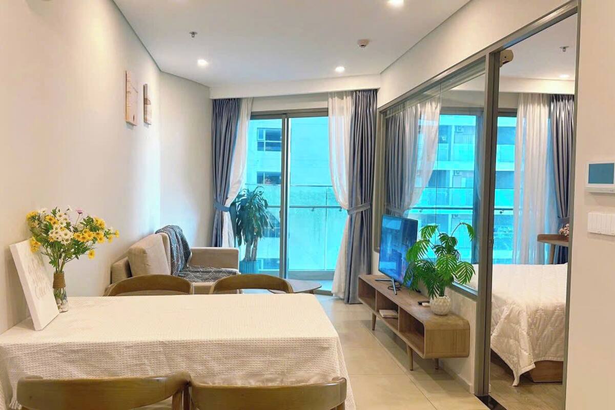 Habitación de hotel con cama, escritorio, silla, televisor y balcón con cortinas.