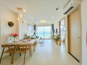 Una sala de estar moderna con comedor, un ventanal con vistas al mar y una puerta corrediza de vidrio que da a un balcón.