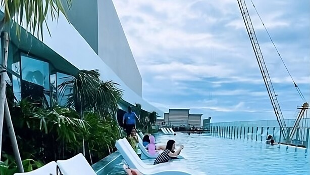 Ein Poolbereich mit Liegestühlen, Palmen und blauem Himmel.