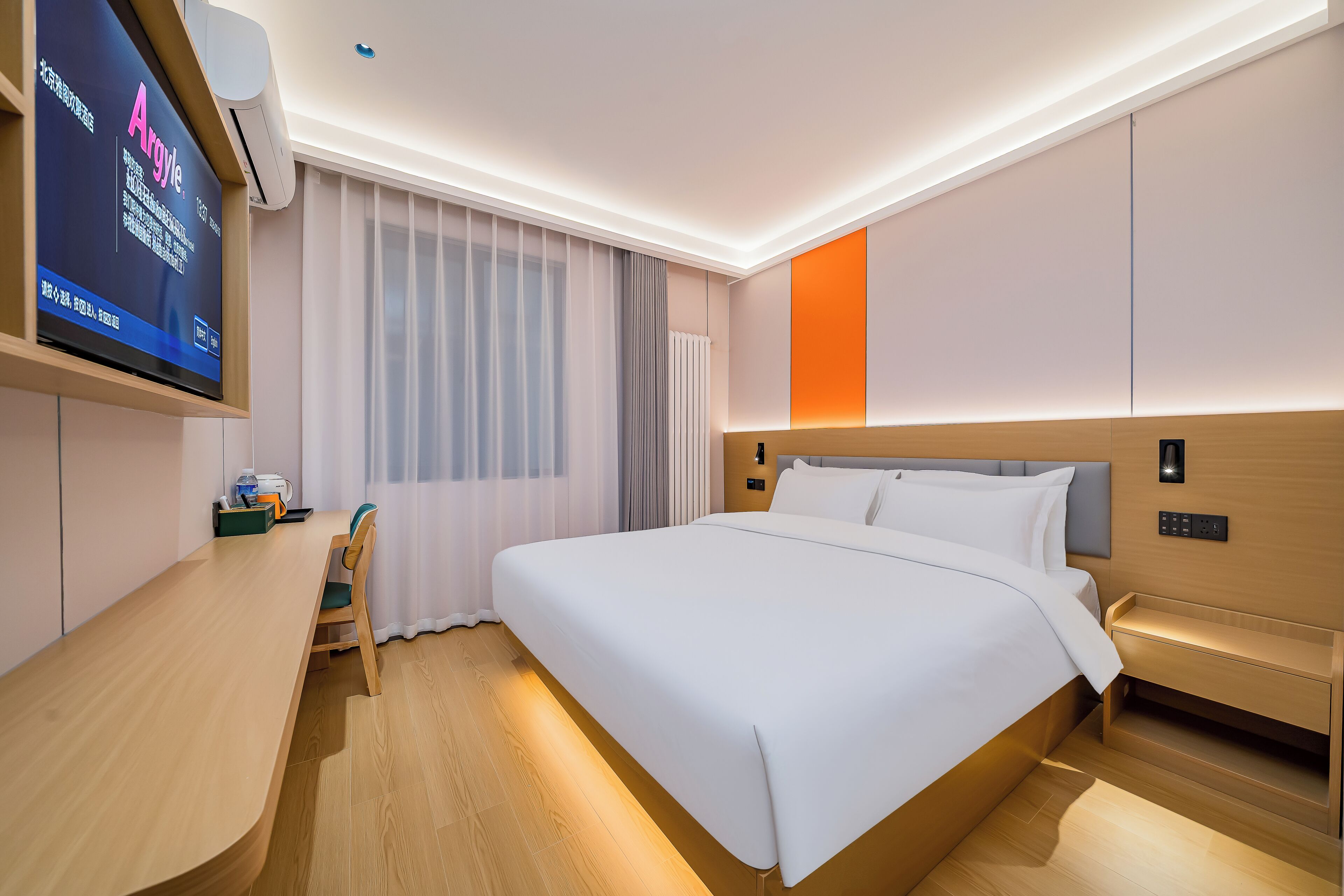 Una habitación de hotel moderna con una cama grande, mesitas de noche, un escritorio y un televisor montado en la pared.