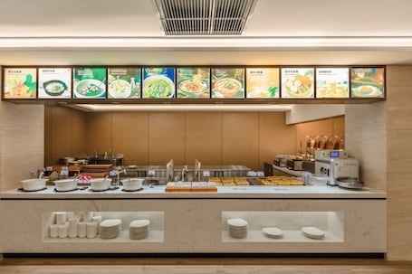 A buffet counter with various dishes, a coffee machine, and a menu above displaying food options.. yagehuanjujiudian