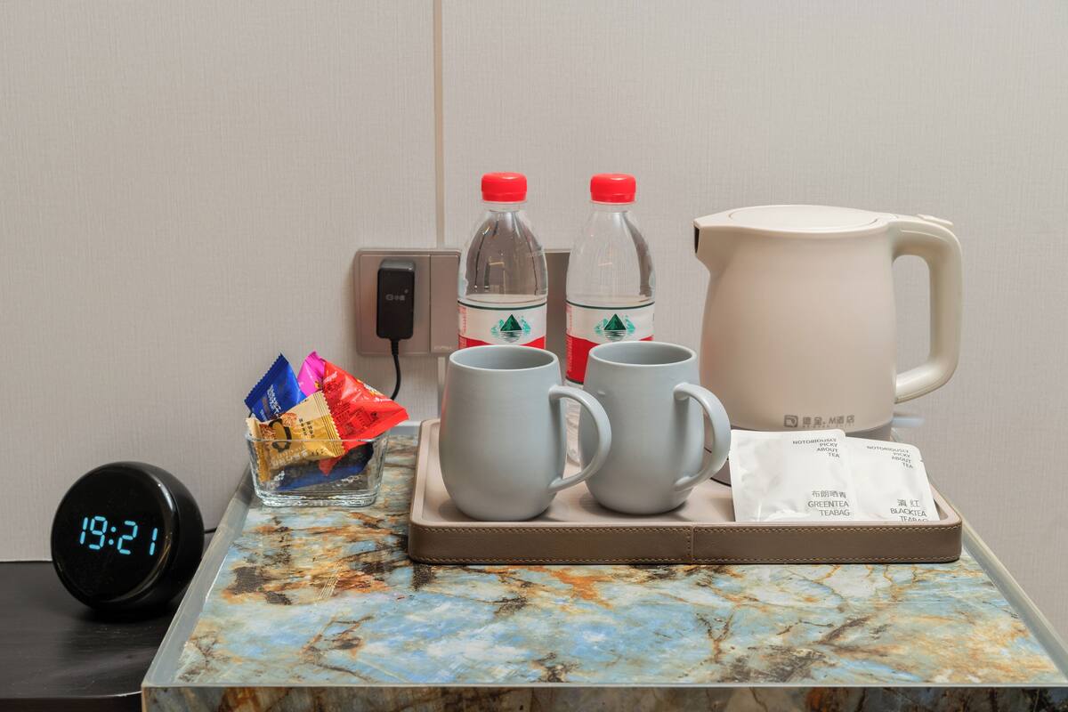Ein Tablett mit zwei Tassen, einem Teekessel, einer Wasserflasche, einem Glas mit Snacks, einer Uhr und einer Steckdose.