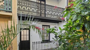 Ein zweistöckiges Gebäude mit aufwendig gestalteten schwarzen Eisengeländern am Balkon, einer schwarzen Tür und einem kleinen Garten mit verschiedenen Pflanzen.