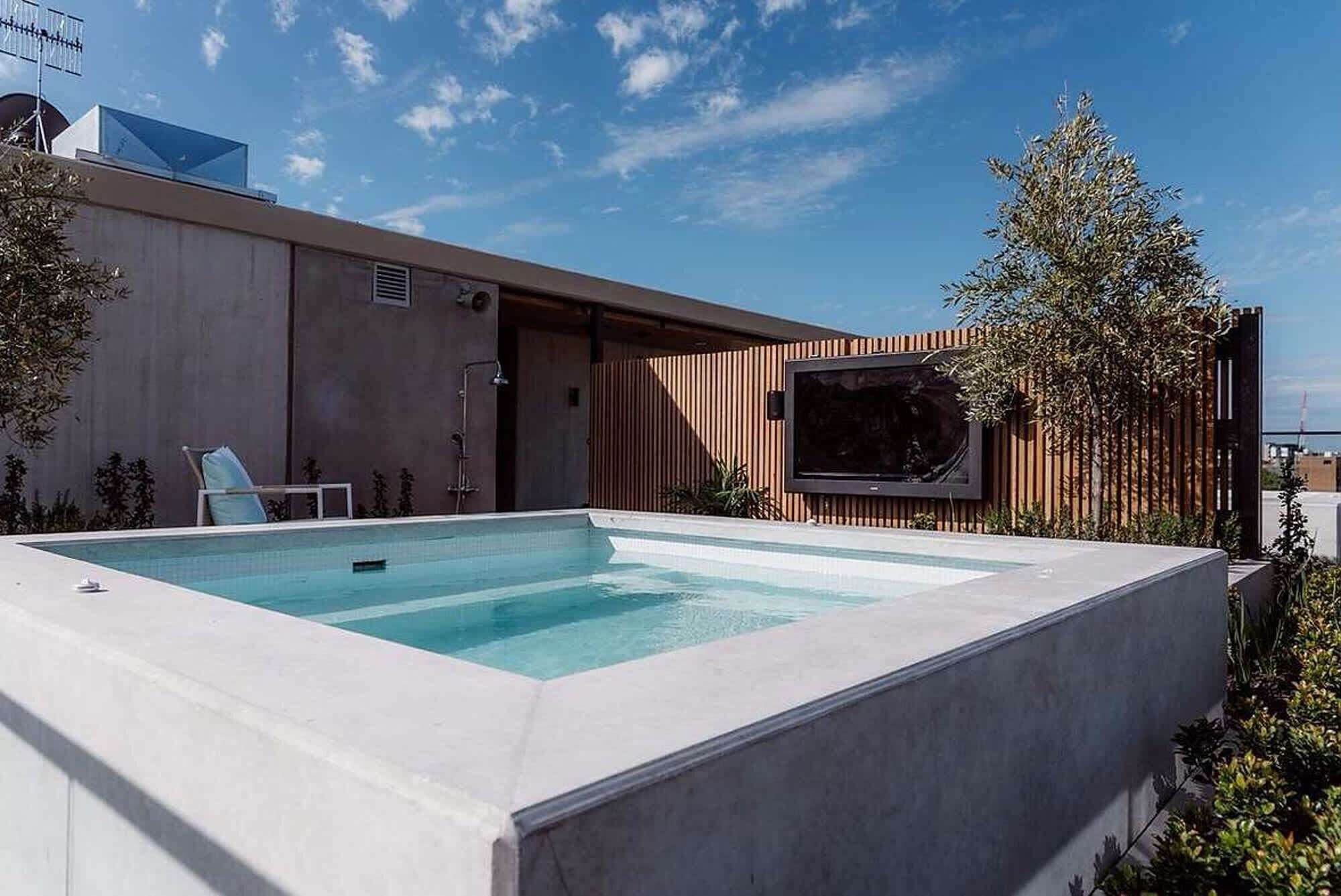 Une piscine rectangulaire au design moderne, une clôture en bois et un téléviseur à écran plat fixé à la clôture.