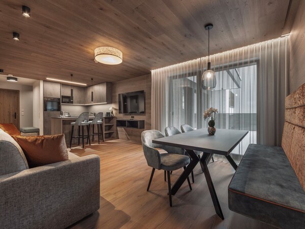 Una sala moderna con comedor, suelo de madera y un amplio ventanal con cortinas.