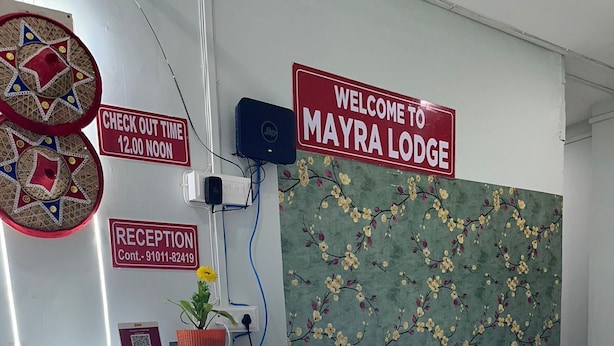 Ein Empfangsschalter mit einem Schild, auf dem 'Welcome to Mayra Lodge' steht, einem Schild mit der Aufschrift 'Check Out Time 12:00 Noon' und einem Schild mit dem Wort 'Empfang' sowie einer Kontaktnummer.