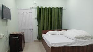 Ein Schlafzimmer mit einem hölzernen Bett, einem Schreibtisch, einem Fernseher und einem grünen Vorhang.