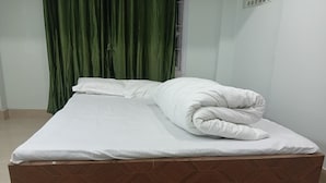 Ein ordentlich bezogenes Bett mit einem hölzernen Kopfteil und einem grünen Vorhang im Hintergrund.