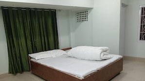Ein Einzelbett mit Holzrahmen und weißer Bettwäsche in einem Zimmer mit heller Bodenbelag und grünen Vorhängen.