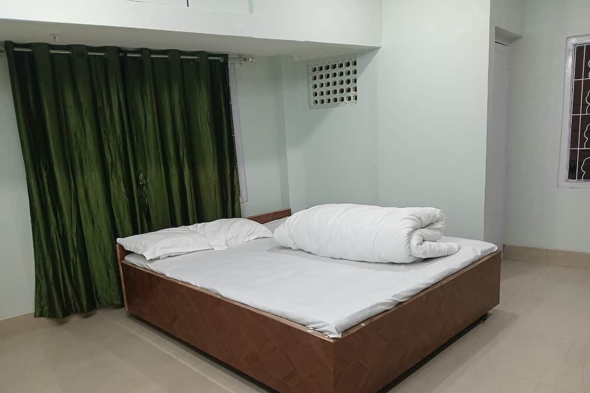 A single bed with a wooden frame and white bedding in a room with light-colored flooring and green curtains.