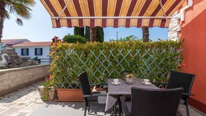 Une terrasse extérieure avec une table et des chaises, un auvent à rayures et une clôture en treillis.