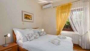 Una camera da letto con un letto, una lampada da comodino, condizionatore d'aria, finestra con tende e un quadro appeso al muro.