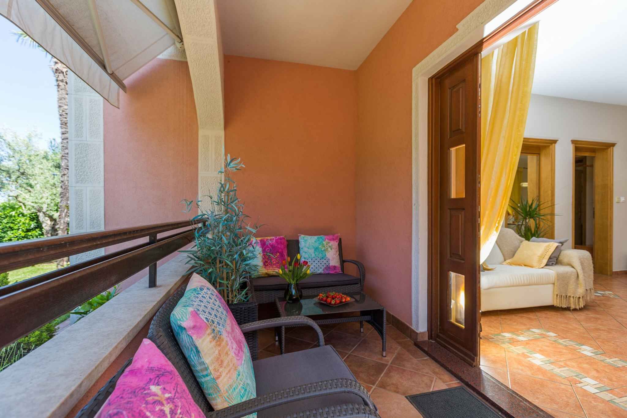 Un balcon avec un canapé, des chaises et une table agrémentée d’un vase de fleurs.