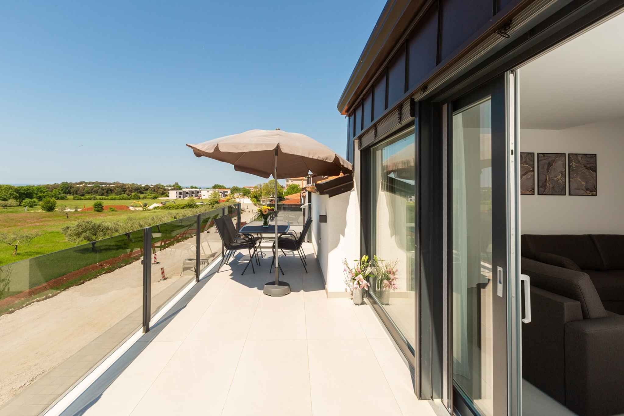 Ein Balkon mit Tisch und Stühlen, einem großen Sonnenschirm und einer Glastür, die zu einem Wohnbereich führt.