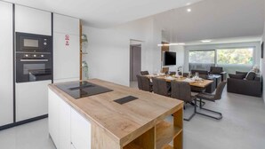 A modern kitchen with built-in appliances, a dining area with a wooden table and chairs, and a seating area with a sofa and a TV. - Holiday apartment with shared pool (Funtana)