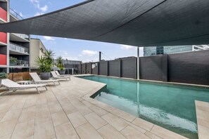 Un espace piscine aménagé sur le toit, avec une partie couverte, des chaises longues et des plantes en pot.
