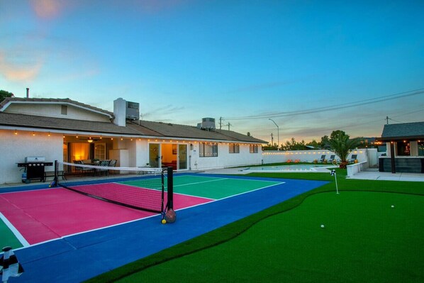 A tennis court with a net, a pool table, and a green lawn area. - Vegas Stays with Games, Volleyball, and More! (North Las Vegas)
