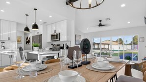 Une cuisine moderne avec des meubles blancs, un coin repas avec une table en bois mise pour le repas, et une vue sur une piscine à l’extérieur.