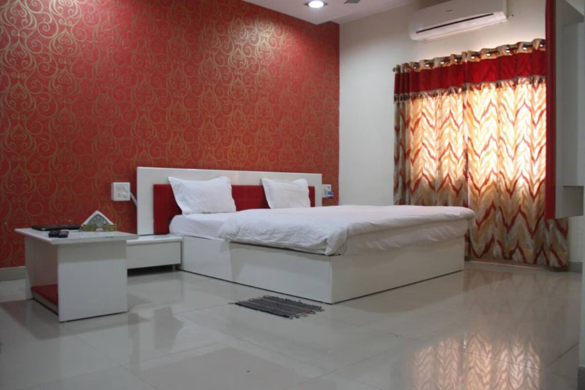 A bedroom with a large bed, white nightstands, a red patterned wall, and a window with a chevron curtain.
