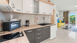 A modern kitchen with a microwave, toaster, and coffee maker on the counter. There is a sink and a window with a view of greenery. - Holiday apartment with air conditioning and Wi-Fi (Poreč)